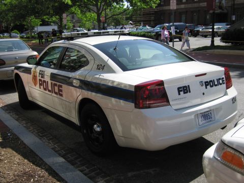 1991 Ford LTD Crown Victoria - Rear three-quarter view of a white Dodge Charger marked FBI POLICE and numbered 124, parked along a tree-lined street.