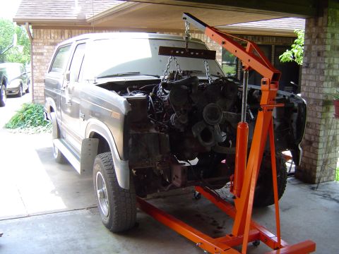 1986 Ford Bronco - An engine hoist is positioned to remove the engine from a Ford Bronco, with another vehicle visible in the background.