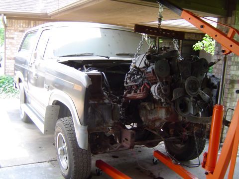 1986 Ford Bronco - An engine is suspended by a hoist, detached from a Ford Bronco in a garage.