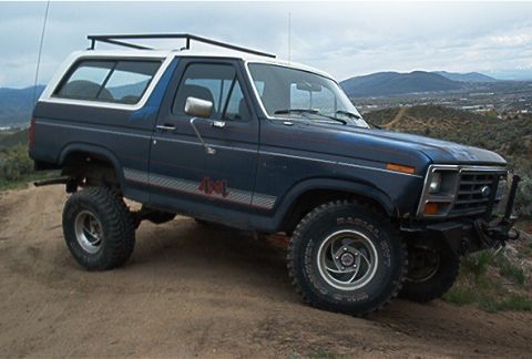 1986 Ford Bronco - This Ford Bronco is parked on a dirt hill with mountains in the background.