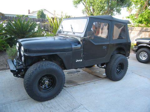 1986 Ford Bronco - This black Jeep CJ7 is shown from the side, a soft top and large off-road tires.