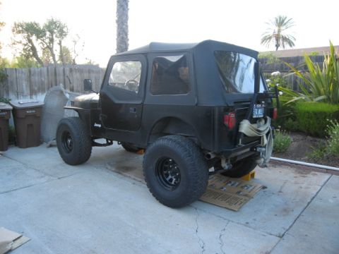 1986 Ford Bronco - This black Jeep CJ7 is viewed from a three-quarter front angle, showing its lifted suspension and off-road tires.