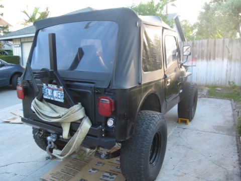 1986 Ford Bronco - This black Jeep CJ7 is viewed from the rear, a soft top and a spare tire carrier.