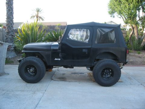 1986 Ford Bronco - A black Jeep CJ is parked in a driveway with a soft top and large tires.