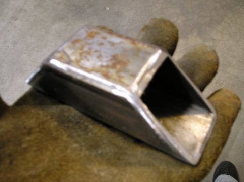 1986 Toyota Hilux - A rusty metal bracket is held in a gloved hand against a concrete floor.