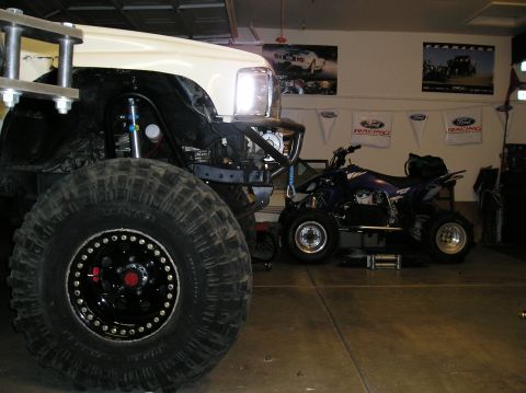 1986 Toyota Hilux - A custom off-road truck with oversized tires is parked next to a blue ATV in a garage setting.
