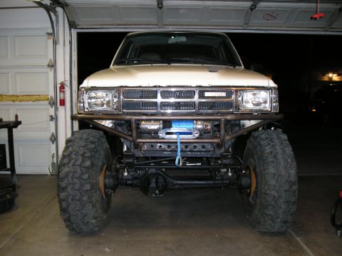1986 Toyota Hilux - Front view of a modified Toyota truck with a winch mounted on a custom bumper, equipped with large off-road tires.