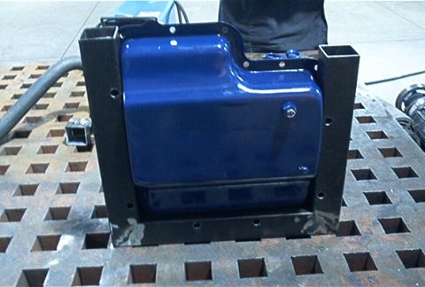 1986 Ford Bronco - A blue transmission skidplate is shown mounted in a black metal frame, resting on a perforated metal surface.