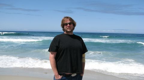 2005 Chrysler PT Cruiser - A man stands on a sandy beach with the ocean and waves behind him.
