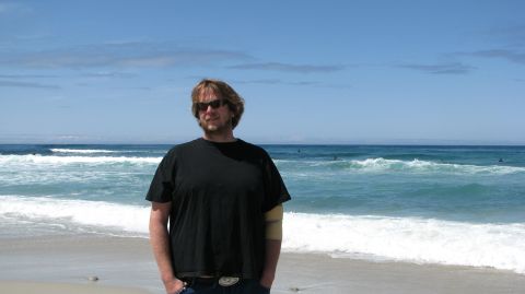 2005 Chrysler PT Cruiser - A man stands on the beach with the ocean and waves behind him.