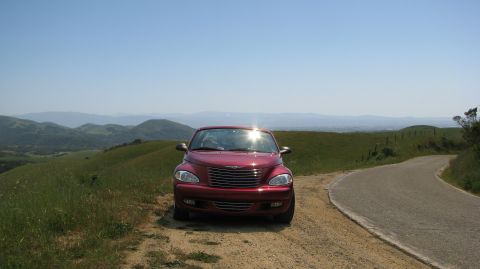 2005 Chrysler PT Cruiser - A red 2005 Chrysler PT Cruiser is parked on a dirt road overlooking a scenic landscape.
