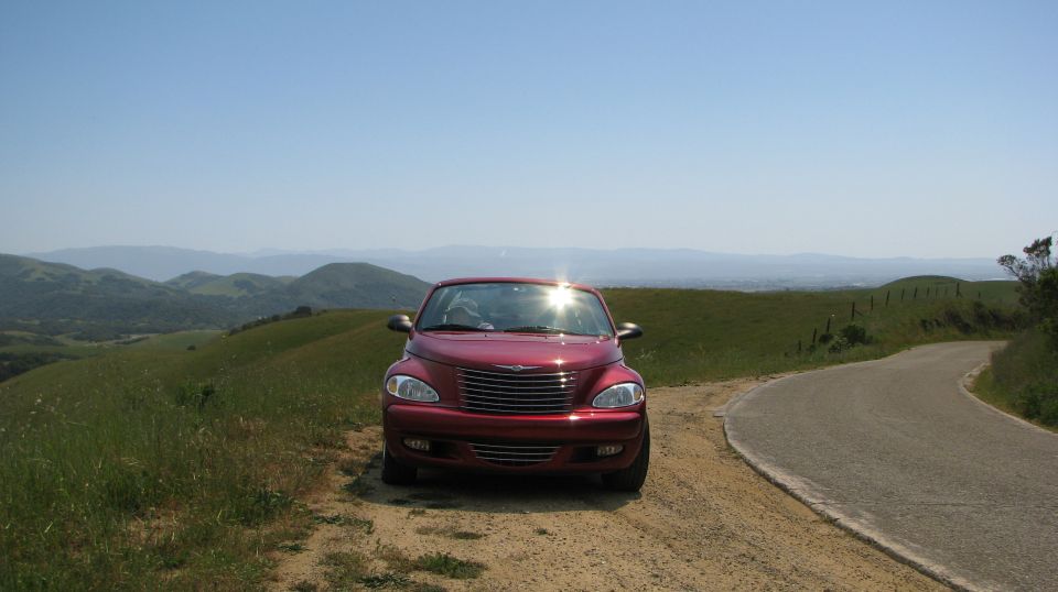 Red 2005 Chrysler PT Cruiser parked on a dirt road with rolling hills and a clear blue sky