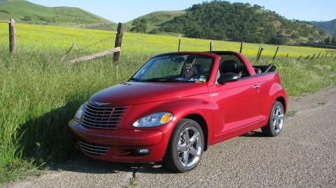 2005 Chrysler PT Cruiser - A red 2005 Chrysler PT Cruiser convertible is parked on the side of a rural road with a field of yellow flowers in the background.
