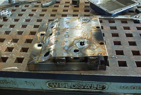1986 Ford Bronco - A damaged metal component rests on a perforated workbench surface.