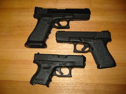 1996 Ford Bronco - Three handguns of varying sizes are arranged on a wooden table. A watermark for "SUPERMOTORS.NET" is visible in the lower right corner.