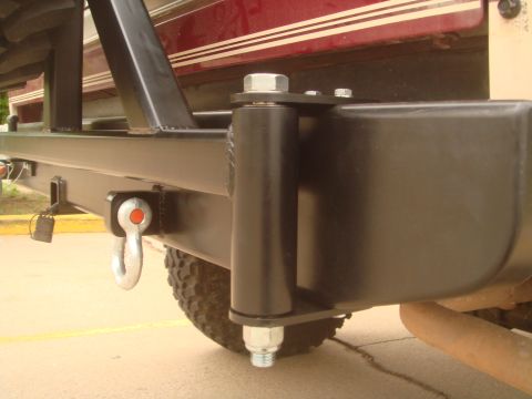 1992 Ford Bronco - Tight low-angle detail of a shop-built black steel rear bumper on a burgundy Ford, focused on the beefy hinge pin and bolt-through pivot of…