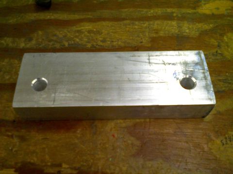 1998 Jeep Cherokee - A rectangular aluminum part with two circular holes is shown on a wooden background.