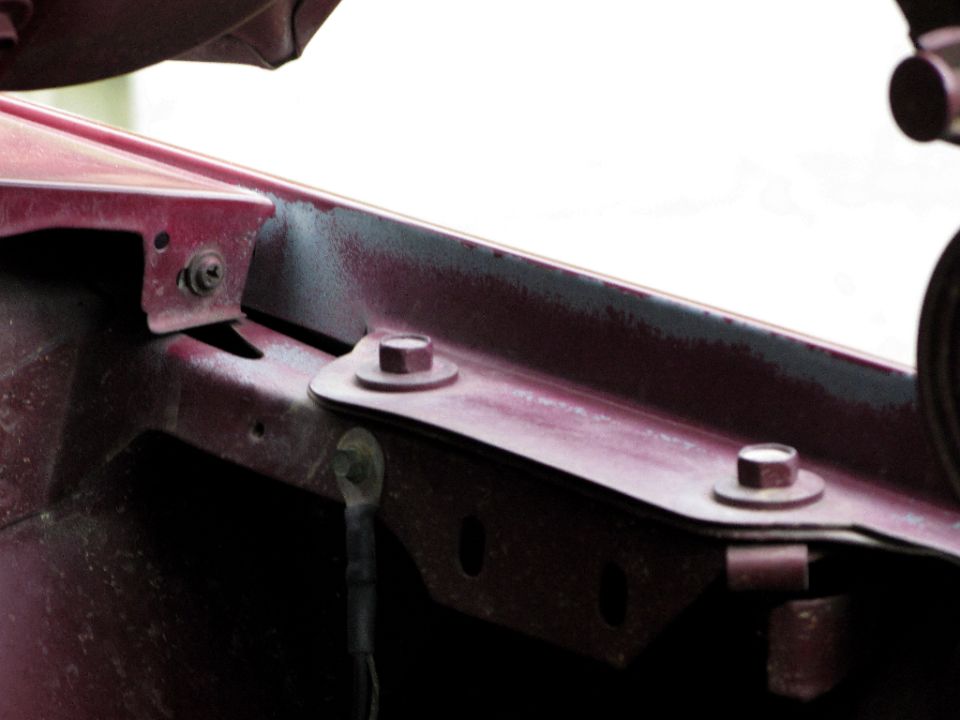 Close-up of a red vehicle's hood hinge area with bolts and brackets