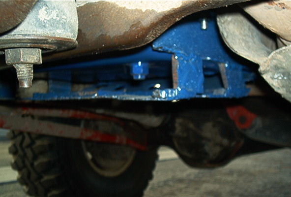 Blue-painted crossmember/skid plate bolted under a truck between rusty frame rails
