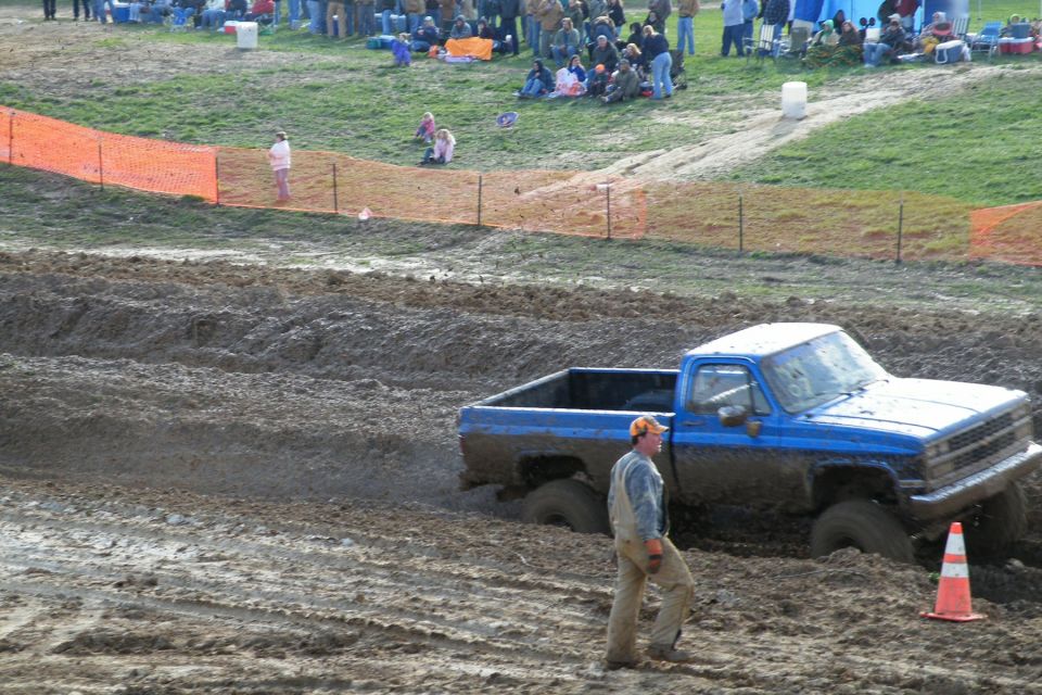 blue pickup truck stuck in mud pit, driver walking nearby