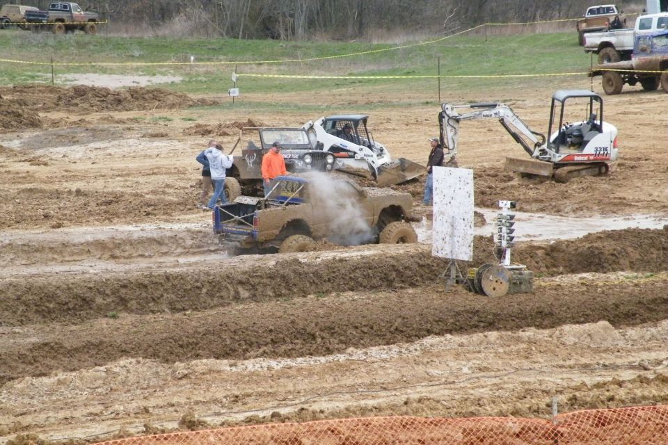 Mud bogging event with a modified truck stuck in mud, a Bobcat loader, and an excavator