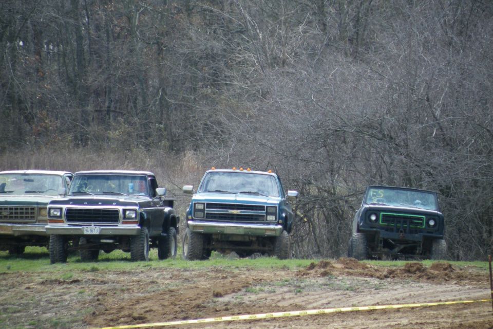Four pickup trucks parked in a line on grassy terrain with trees in the background