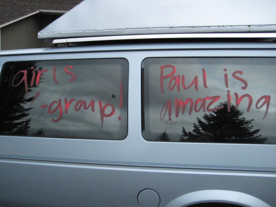 Silver van rear windows with red writing: "girls - group!" and "Paul is amazing".