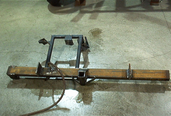 Home-built steel rear bumper with receiver hitch and welded frame brackets on shop floor