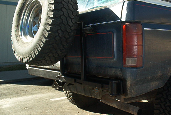 Rear bumper and swing-out spare tire carrier on a dark blue Ford Bronco with red pinstripe
