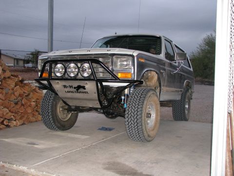 1980 Ford Bronco - A modified 1980s Ford Bronco is parked on a concrete surface in front of a pile of firewood. The front of the vehicle features a custom bum…