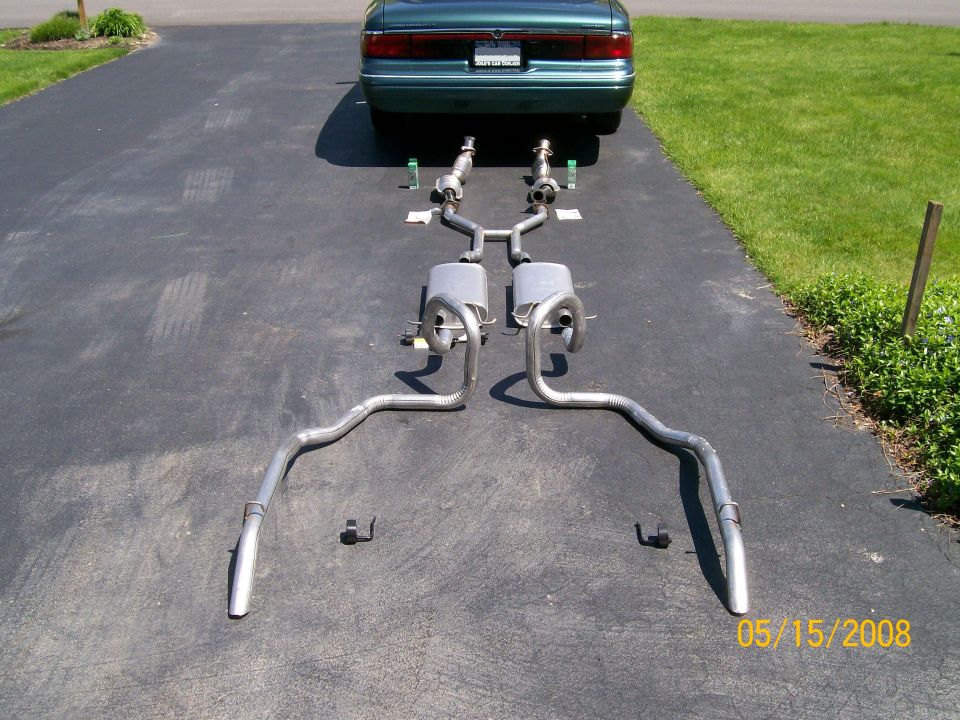 Dual stainless exhaust system laid out on driveway behind green sedan