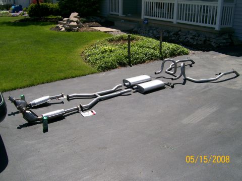 1995 Mercury Grand Marquis - A complete stainless steel dual exhaust system laid out on an asphalt driveway, including two catalytic converters, resonators, two large m…