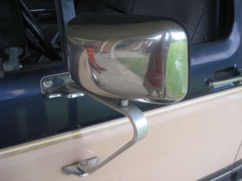 1981 Ford Bronco - Close-up of a chrome swing-arm West Coast style side mirror mounted to the door of a two-tone blue-over-tan truck, with the pinstripe body…