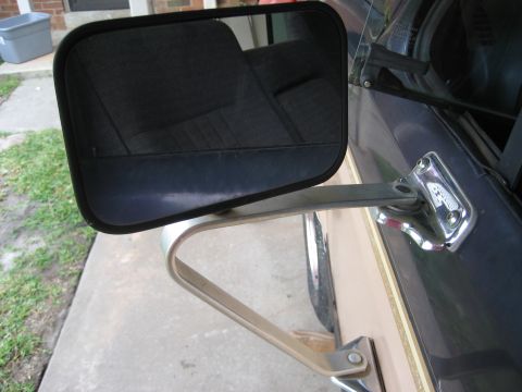 1981 Ford Bronco - A close-up view of a side mirror assembly attached to the door of a dark colored vehicle. The mirror housing is black and reflects the inte…