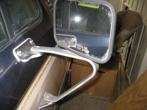 1981 Ford Bronco - A close-up view of the driver's side exterior mirror assembly mounted on a dark-colored vehicle door. The mirror housing has text that read…