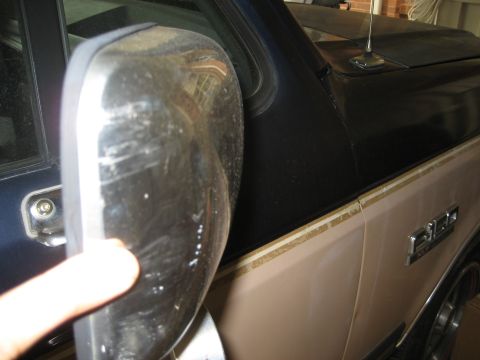 1981 Ford Bronco - A close-up view of the driver's side mirror and front fender of a two-tone beige and dark blue pickup truck. The chrome mirror housing is s…