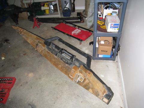 1996 Ford Bronco - A heavily rusted, custom-fabricated steel bumper is laid out on a concrete garage floor next to a red tool chest and a gray plastic shelvin…