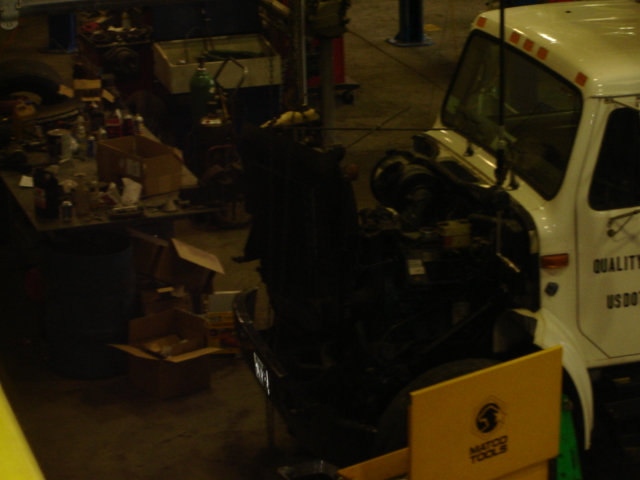 Dark shop photo of a truck with engine and cab partly disassembled