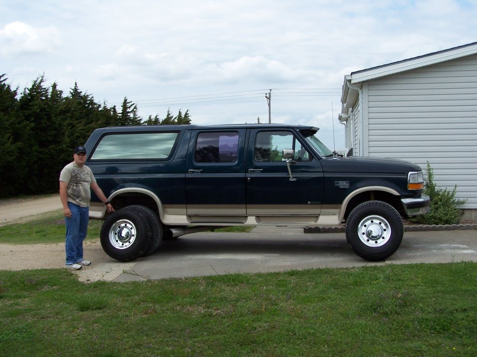 Man standing next to a dark green Ford Bronco with tan trim.