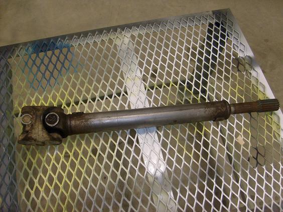 Rusty driveshaft with a universal joint and splined end on a diamond plate surface.