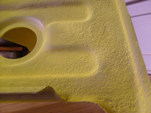 Close-up of textured yellow vehicle part with embossed contours and a circular cutout.