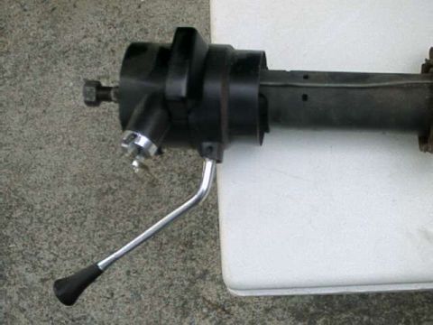 1976 Ford Ranchero - A close-up view of a black steering column assembly with a silver lever and black handle. The assembly is resting on a white surface with a…
