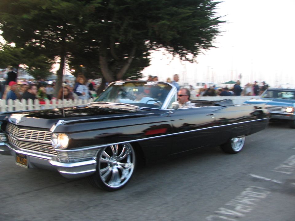Black vintage convertible Cadillac driving with people on the sidewalk.