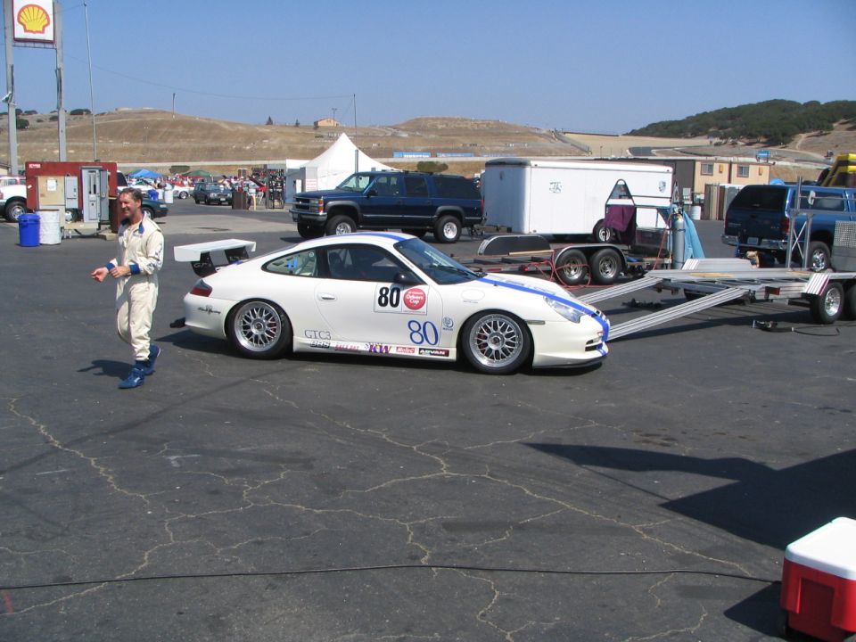 White Porsche 911 GT3 race car with blue stripes and number 80, parked on asphalt.