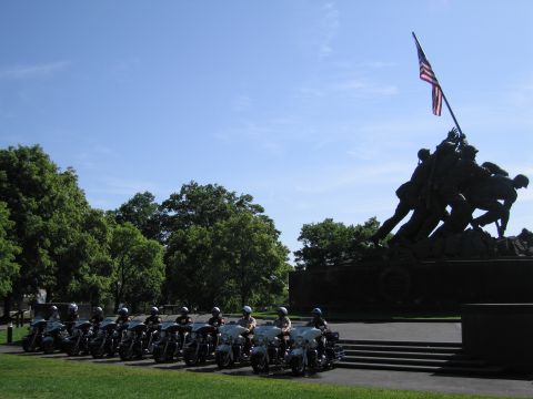 1991 Ford LTD Crown Victoria - row of police motorcycles sits on grass before the bronze Iwo Jima flag-raising memorial against a blue sky.