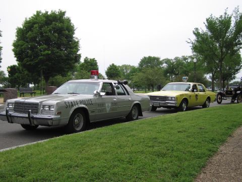 1991 Ford LTD Crown Victoria - silver STATE POLICE sedan with roof beacon sits ahead of a yellow police car in a row of cruisers.