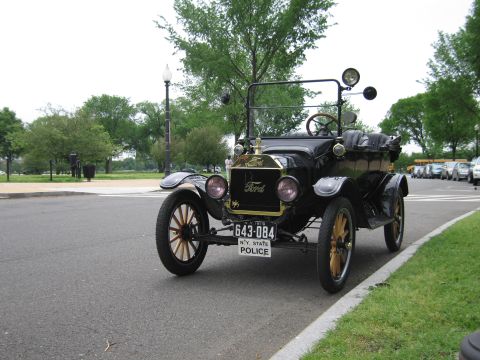 1991 Ford LTD Crown Victoria - black brass-era Ford Model T touring car lettered N.Y. STATE POLICE parked on a park road, viewed from the front.