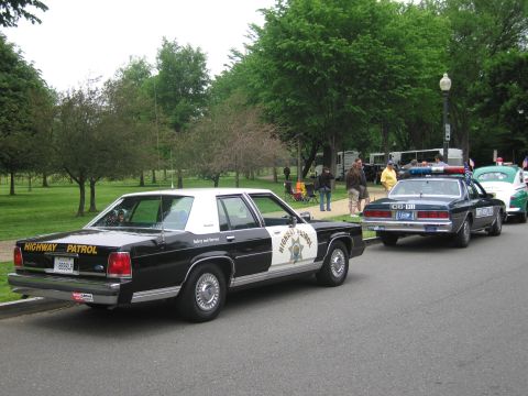 1991 Ford LTD Crown Victoria - black-and-white HIGHWAY PATROL sedan with star emblem leads a row of parked police cars on a park road.