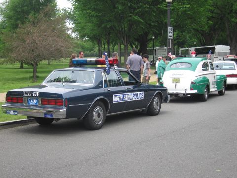 1991 Ford LTD Crown Victoria - dark blue NORTH HAVEN POLICE sedan parked in a line ahead of a green vintage coupe along a park road.