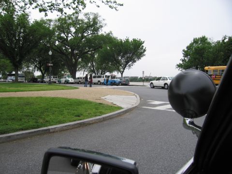 1991 Ford LTD Crown Victoria - grassy roadside parking area holds several vans and cars, seen past a black motorcycle mirror with a yellow school bus at right.